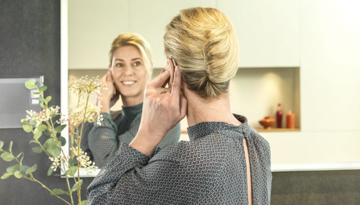 Bernafon: Frau mit Hinter-Dem-Ohr-Hörgerät schaut in den Spiegel