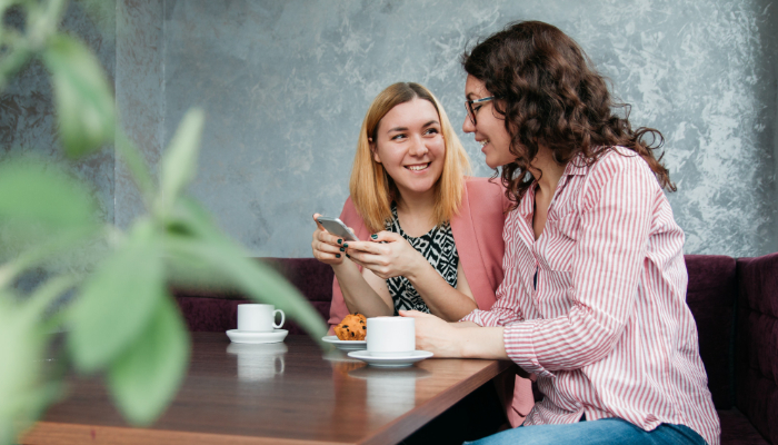 Oticon: Zwei Frauen mit Smartphone am Tisch eines Cafés im Gespräch