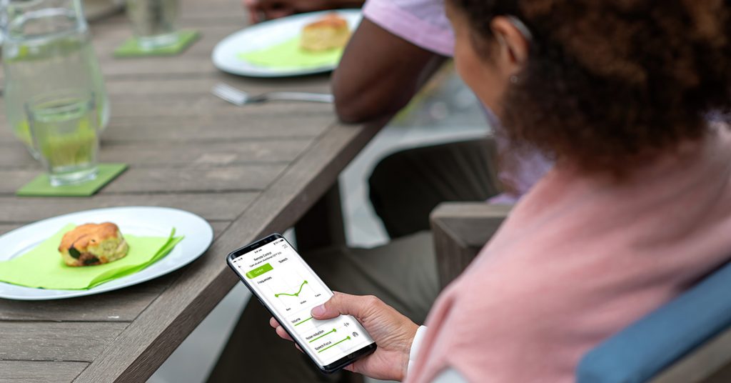 Eine Frau steuert Hörgeräte mit dem Smartphone