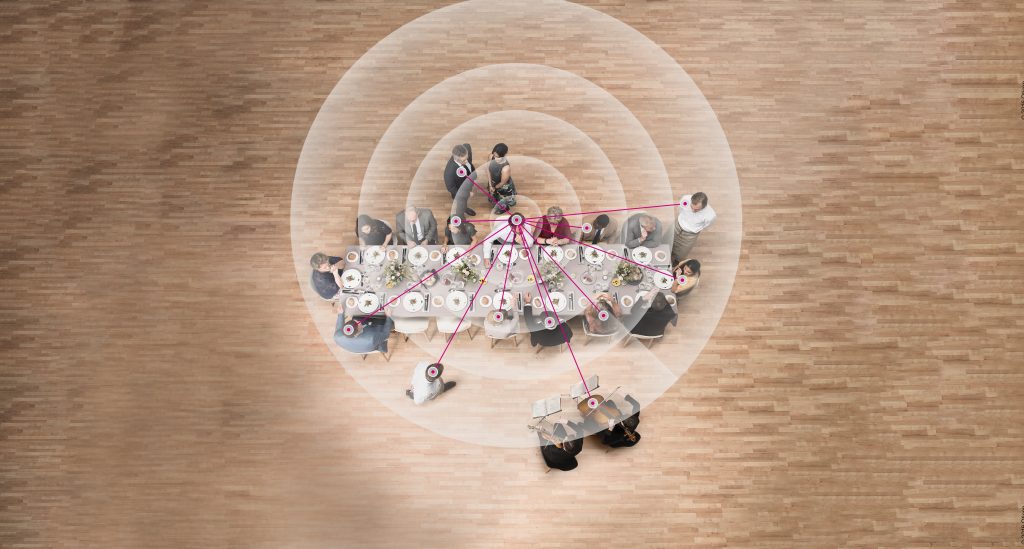 Blick von oben auf einen langen Tisch, an dem mehrere Menschen sitzen. Schallwellen und Linien symbolisieren die Arbeitsweise von Richtmikrofonen.