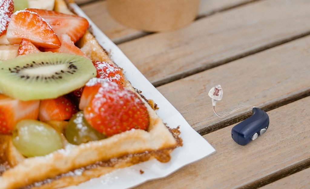Ein Bernafon Alpha Hörgerät auf dem Tisch neben einem Stück Kuchen.
