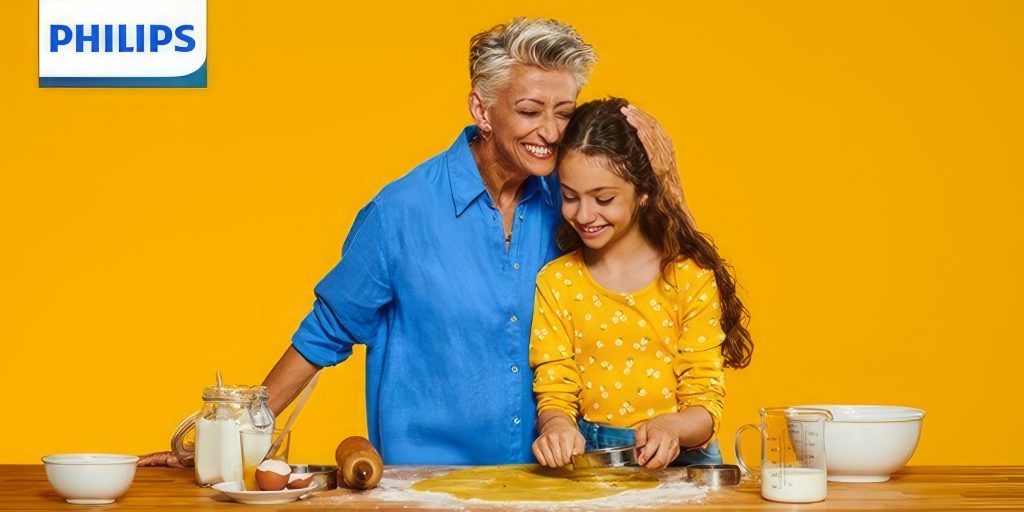 Eine Frau und ein Kind in der Küche unter einem Logo für Philips Hörgeräte