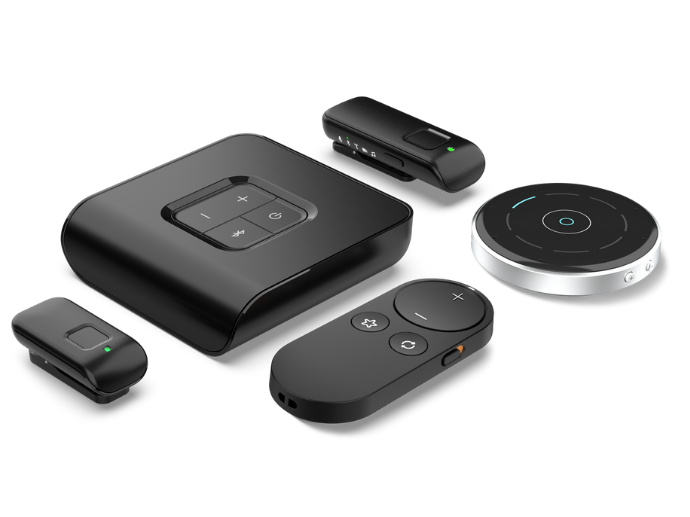 Verschiedene moderne Hörgeräte-Zubehörteile in elegantem schwarzen Design sind auf weißem Hintergrund arrangiert. Die Geräte umfassen unter anderem eine Fernbedienung, ein Remote-Mikrofon, ein Konferenzmikrofon und einen TV-Adapter – alle mit klaren Bedienelementen und minimalistischer Gestaltung für die kabellose Kommunikation und Steuerung von Hörhilfen.
