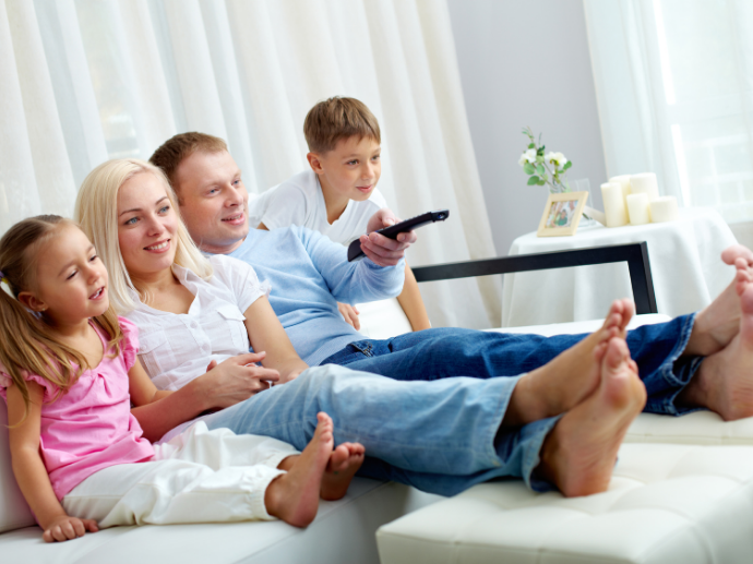 Familie sitzt beim TV, einer trägt Bluetooth-Hörgeräte.